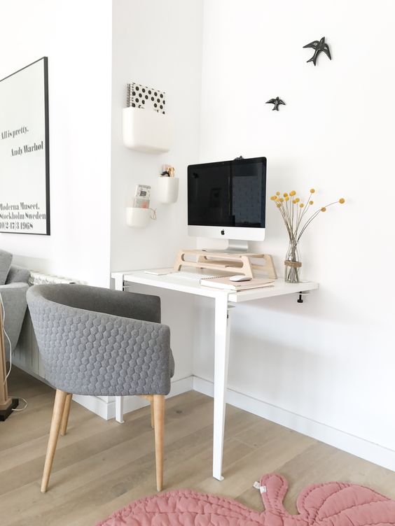 A working nook with a two leg desk, a grey chair, a PC on a stand for more comfort and a series of box like shelves