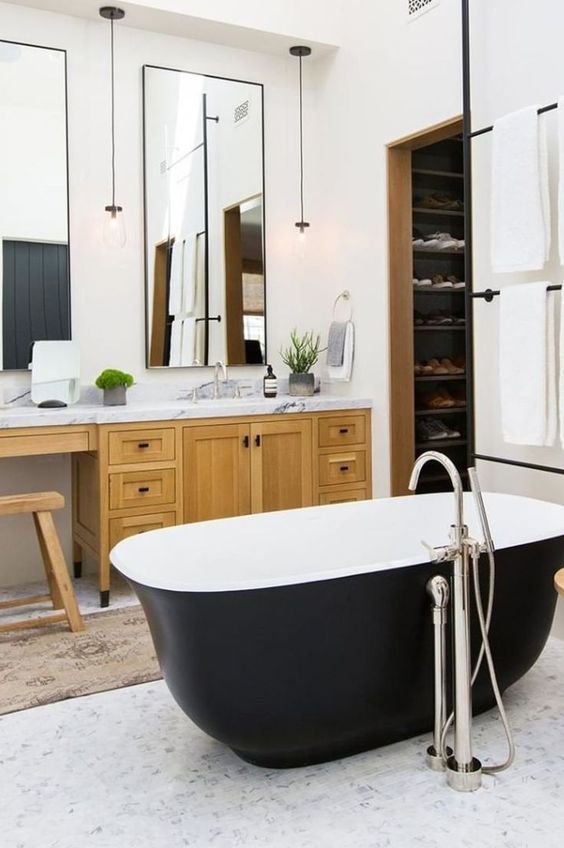 A farmhouse bathroom with a light stained vanity, a couple of mirrors, a matte black bathtub and pendant lamps