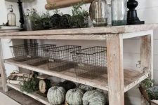 a farmhouse whitewashed console with green whitewashed pumpkins, greenery, wire baskets and lamps