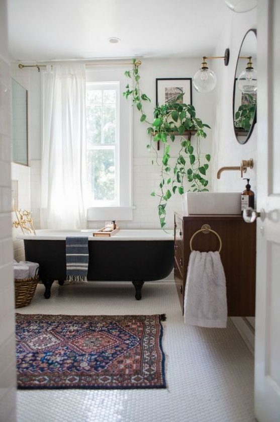 a mid-century modern bathroom with white subway tiles and penny ones, with a black clawfoot tub, a floating vanity and potted plants