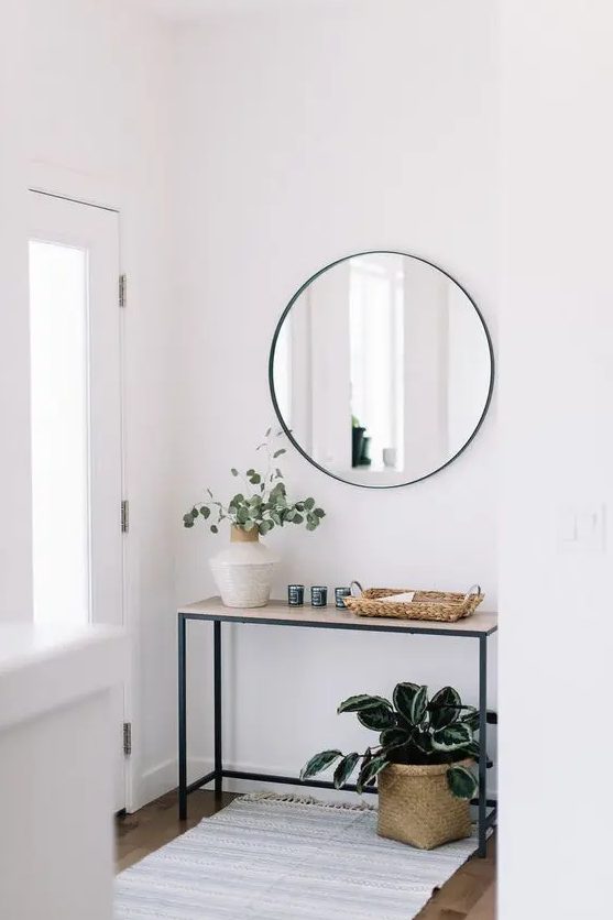 A minimalist console table with a vase with greenery, a wicker catch all, a basket planter under the console
