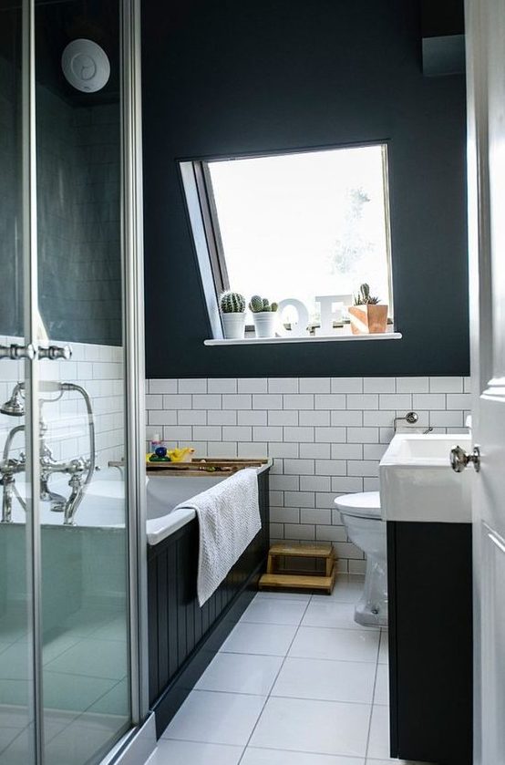 a modern black and white attic bathroom with a bathtub clad with black palnks, a black vanity with a white sink, a square tile floor