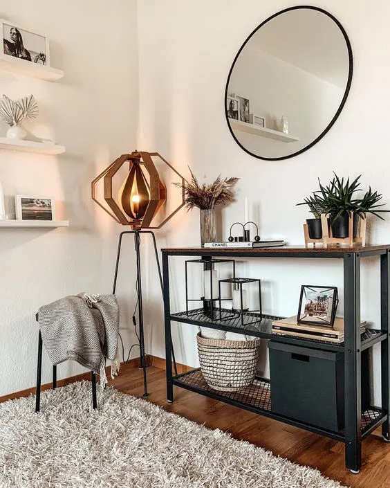 A modern metal and wood console table, potted plants, grass in a vase, some candleholders, a box and a basket plus a very eye catchy floor lamp