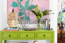 a super bright neon green console with a birdcage candle holder, greenery, a bold artwork and a basket with colorful textiles