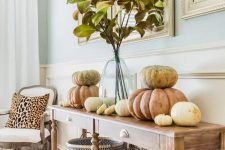 a vintage farmhouse console table with chevron baskets, natural pumpkins stacked on each other and fall leaves in a vase