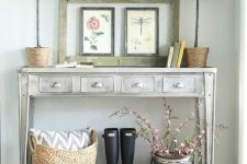 a whitewashed metal console table, a gallery wall of vintage biology posters, potted plants, books, rubber boots and a bucket with faux cherry blossom