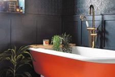 10 a refined moody bathroom with black walls and paneling, an orange clawfoot bathtub, potted greenery and candles is wow