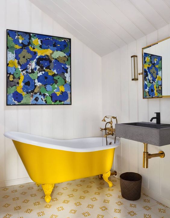 A small attic bathroom with white shiplap, a yellow clawfoot bathtub, a wall mounted sink, a bright artwork and a mirror