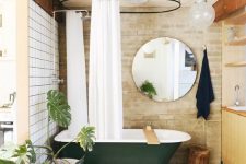 14 a stylish bathroom with white tiles and brick walls, a dark green clawfoot bathtub, a round mirror, a wooden vanity and potted plants