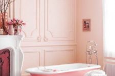 22 a lovely girlish bathroom with blush paneled walls, a vintage fireplace, a pink clawfoot bathtub, a shabby chic chair and some blooms