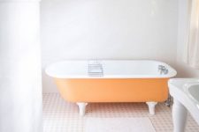 23 a light-filled bathroom with light blue walls, an orange clawfoot bathtub, a crystal chandelier and a vintage gallery wall