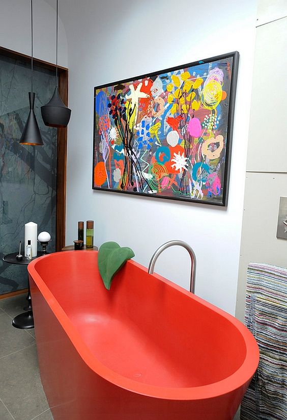 a super bold and catchy bathroom with a hot red free-standing bathtub, a bright artwork and black pendant lamps, small side tables and colorful towels