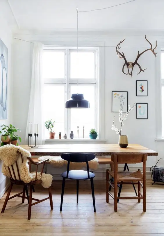 A Scandinavian dining space with a wooden bench and table of mid century modern style, stained and painted chairs and a black pendant lamp