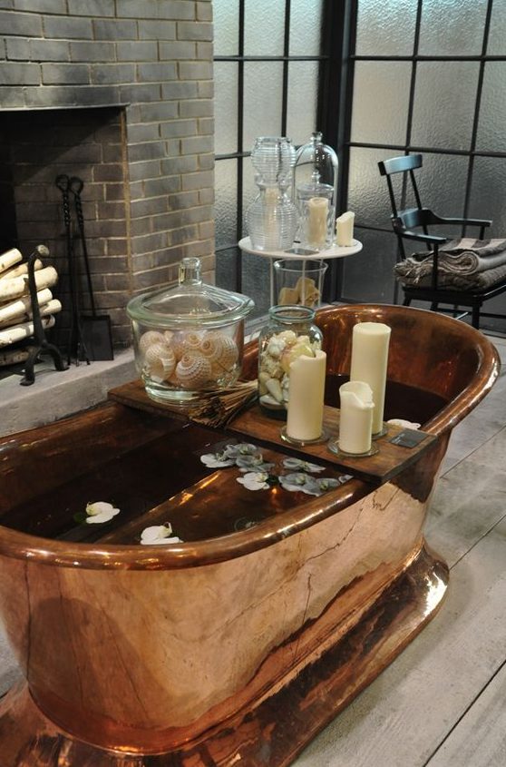 A beautiful bathroom with a non working fireplace, elegant furniture, a copper bathtub and candles all around