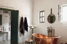a beautiful vintage bathroom clad with white bricks, a copper bathtub that takes a center stage, a candelabra, a round mirror and a graphic rug