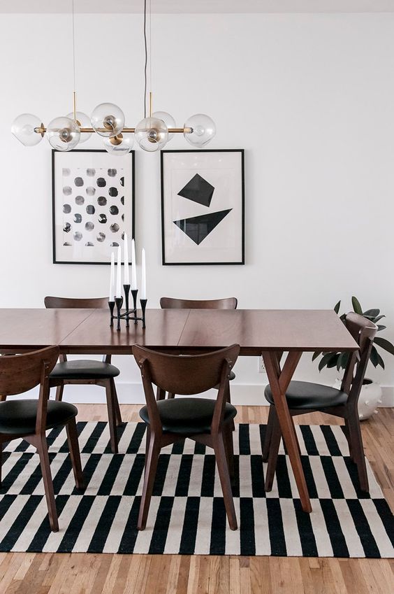 A bold black and white mid century modern dining space with a stained table and black chairs, a striped rug and a gallery wall