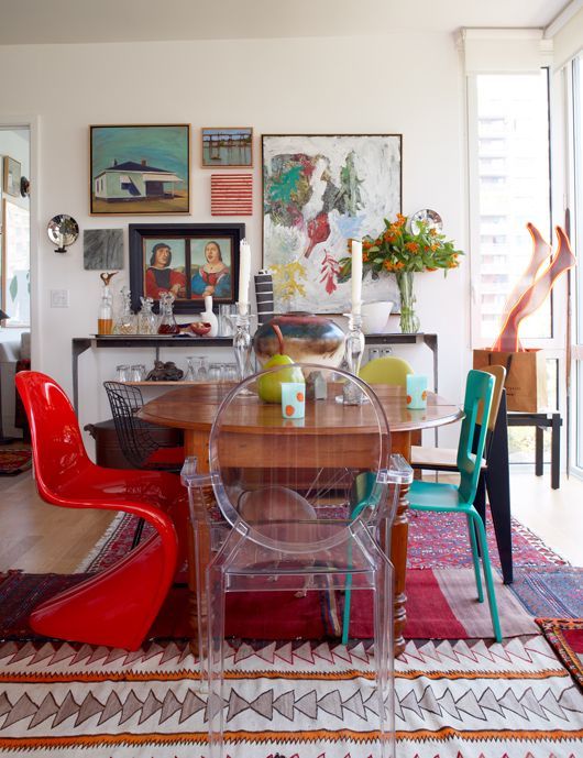 a bright dining space with a vintage wooden table, bright mismatching modern and contemporary chairs, acrylic chairs, colorful printed rugs