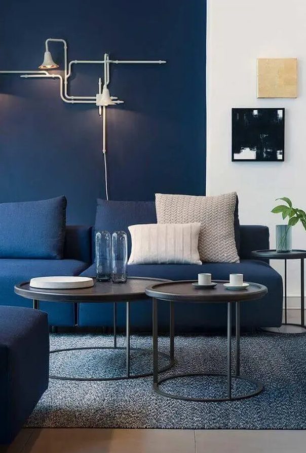 A bright modern living room with navy walls, navy sofas, black side tables and cool art, unique industrial inspired sconces