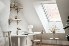 a chic attic home office with a white desk and neutral chair, some shelves, a tall stool and some dried blooms on a stand