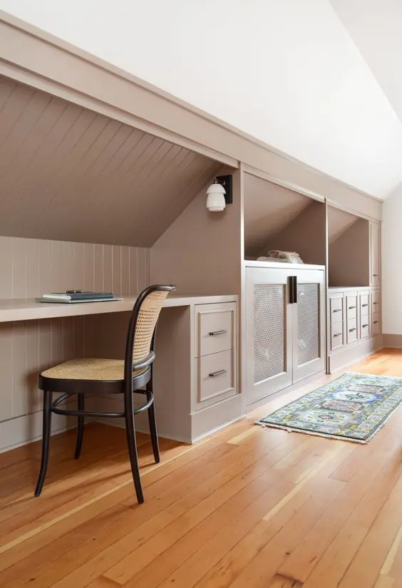 a cool attic space featuring built-in storage with drawers and cabinets, a desk and a cane chair looks awesome