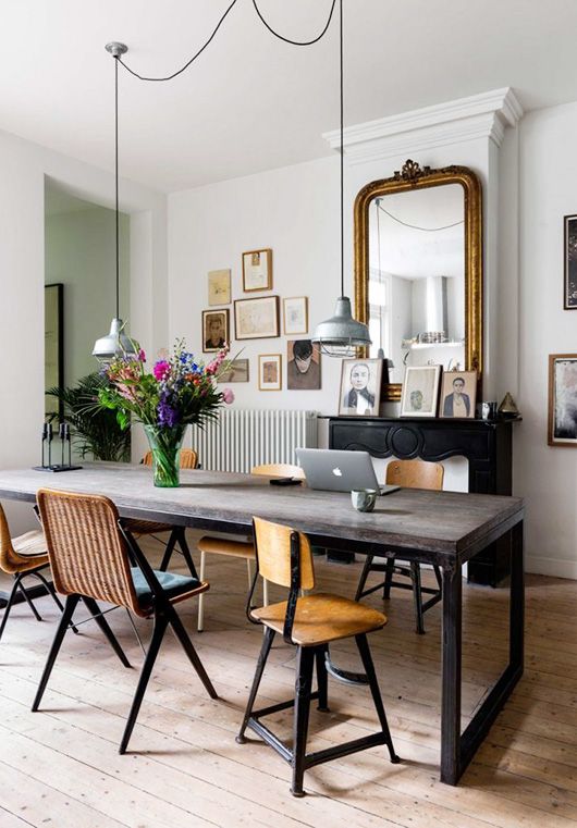 A creative dining room with a faux fireplace, an industrial dining table, mid century modern and industrial chairs and industrial lamps