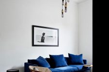 a dreamy living room done in contrasting colors, with a navy sofa, cane chairs, round side tables and bulbs hanging from the ceiling medallion