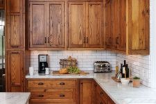 a farmhouse kitchen with rich-stained shaker cabinets, white stone countertops and a white subway tile backsplash is very cozy