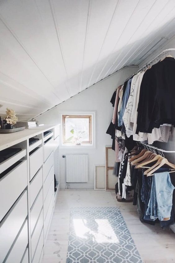a functional attic closet with dressers, railings with clothes, artwork and a rug is a lovely and cool space to be in