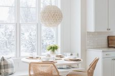a light-filled breakfast nook with a modern built-in bench with pillows, a vintage round table and rustic woven chairs plus a pendant lamp