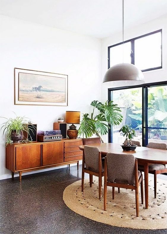 a lovely mid-century modern dining space with a stained table, grey chairs, a credenza and some plants plus a round jute rug