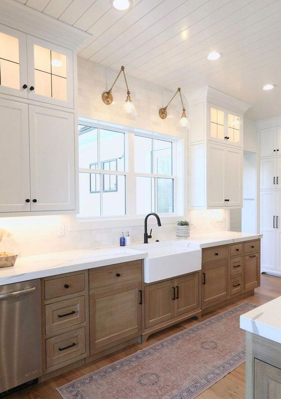 a modern farmhouse kitchen with white upper cabinets and stained lower ones, with black handles and white stone countertops