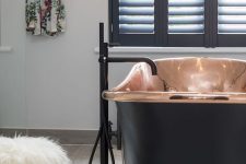 a modern luxurious bathroom with a copper and black bathtub for a statement, black shutters and black fixtures