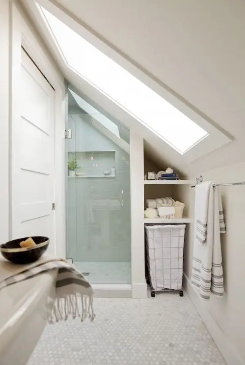 a neutral attic bathroom with a shower space done with aqua tiles, penny marble tiles on the floor and a large skylight
