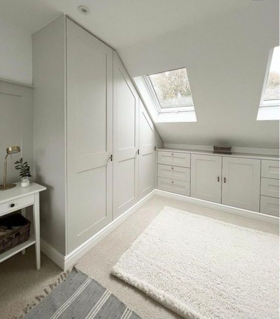 A neutral attic closet with built in wardrobes, cabinets and drawers, skylights and rugs for more coziness is a cool space