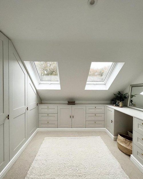 A neutral attic closet with wardrobes, built in drawers and storage compartments and a vanity with a mirror is amazing