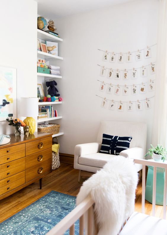 A pretty and cozy neutral nursery with open built in shelves, a stained credenza for storage, a creamy chair, a white crib and printed textiles