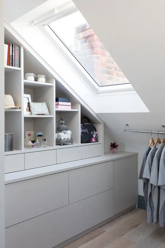 a small attic closet with open storage compartments and cabinets and drawers, a rail with clothes is a smart and cool idea