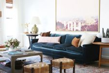a stylish and elegant living room with a navy vlevet sofa, a statement artwork, a coffee table and woven stools, neutral pillows