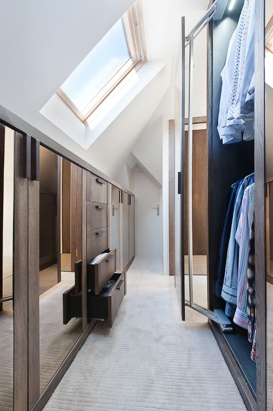 A stylish and light filled attic closet with well organized wardrobes with ,oving doors and a cool storage unit with drawers and mirrors