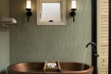 a stylish bathroom wiht green tiles, large scale ones on the floor, an oval copper bathtub, black fixtures and a glazed wall