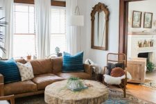 a stylish farmhouse living room with a modern brown leather sofa, a rustic living edge table with hairpin legs, rattan chairs and a mirror in a wooden frame plus a boho rug