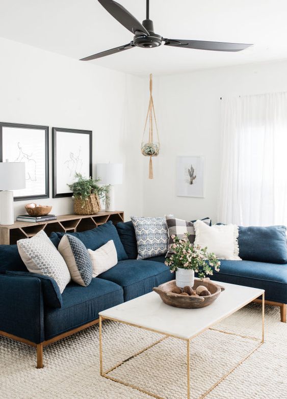 A stylish mid century modern neutral living room with a navy sectional, a coffee table, a lovely credenza, some pretty artwork and potted greenery and blooms