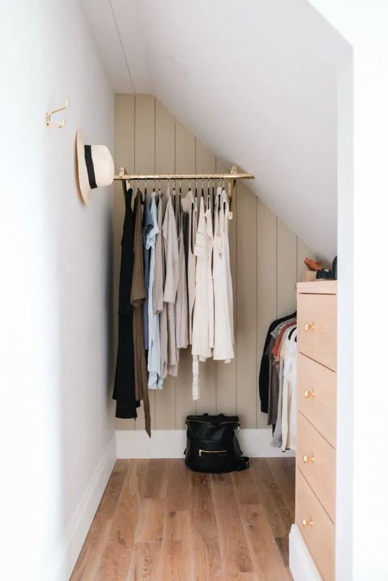 a tiny attic nook with railings for hanging clothes, a blush dresser and some hooks on the walls is awesome