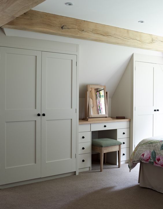 a welcoming neutral bedroom with built in attic wardrobes and a small desk that doubles as a vanity