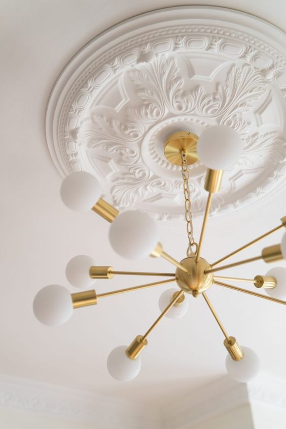 A white ceiling medallion with a gold sunburst chandelier   the vintage look of the medallion and modern look of the chandelier contrast