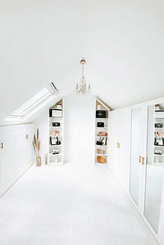 An all white attic closet with open shelves, closed storage compartments, an elegant chandelier, some decor and mirrors