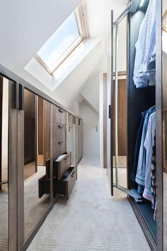 An attic closet with elegant stained built ins with mirrors and drawers and super tall racks for hanging clothes