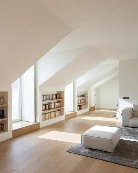 an attic living room with built-in bookshelves, windows, neutral seating furniture and a grey rug looks airy and ethereal