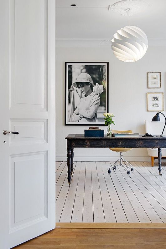 an eclectic home office with a shabby navy desk, a plywood chair, a gallery wall and a swirl pendant lamp and lots of natural light