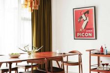 an elegant and refined mid-century modern dining room with a long table and black chairs, a bar cart, green curtains, an amber glass chandelier and a print